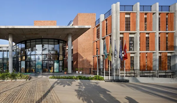 EuroSchool Bannerghatta, Bangalore — brick and timber-louvred campus block with a curved glazed entrance canopy and a row of flagpoles