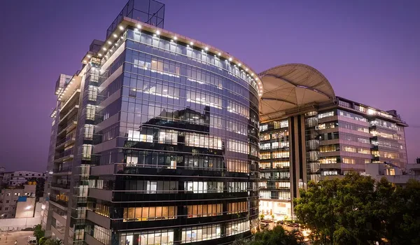 Kalyani Magnum Tech Park, Bangalore — curved glass office building with lit floors at dusk and a canopied block alongside