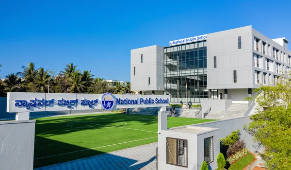 National Public School, JP Nagar, Bangalore — the school name in Kannada and English on the boundary wall beside the turf field, with the classroom block behind