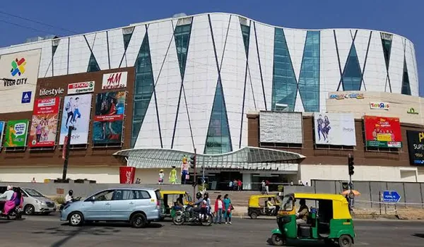 Nexus Vega City Mall on Bannerghatta Road near Nambiar Beverly Park, a white curved-glass mall with Lifestyle, SPAR and H&M signage and traffic on the road in front